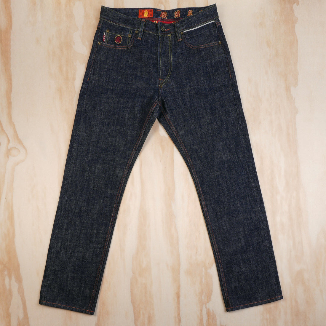 5KM Year of the Horse dark indigo selvedge jeans laid flat, showing the front pockets and red waistband details.