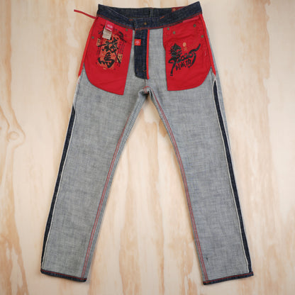 A pair of gray denim jeans with red patch pocket lining featuring black graphic prints, laid flat on a light wood background. 
