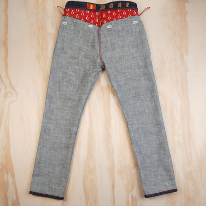 A pair of inside out selvedge denim jeans laid flat on a light wood background, featuring a highly decorative red waistband with gold and blue patterns.