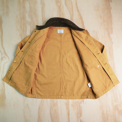 A khaki canvas chore coat with a dark brown corduroy collar, laid flat opned on a light wood background. Showing internal felled seams and unlined.