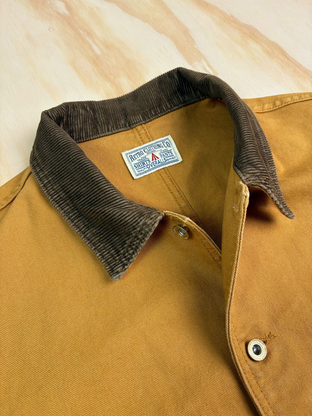 Close-up of a Khaki cotton canvas Chore coat with a dark brown corduroy collar, showing the interior neck label.