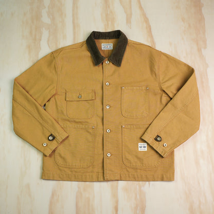 A classic khaki canvas chore coat with a dark brown corduroy collar, laid flat on a light plywood background.