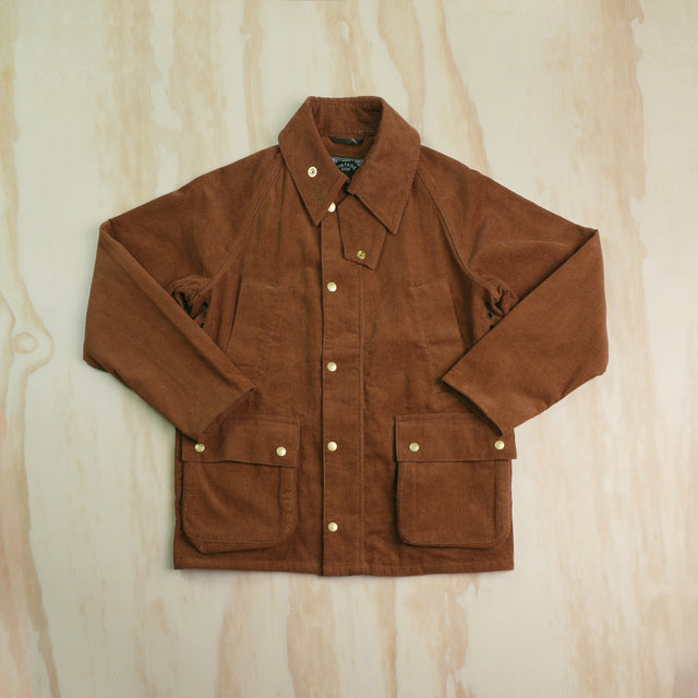 A brown corduroy hunting jacket with a pointed collar, button-up front, two handwarmer pockets and two front flap pockets, laid flat on a light wood-grained background.