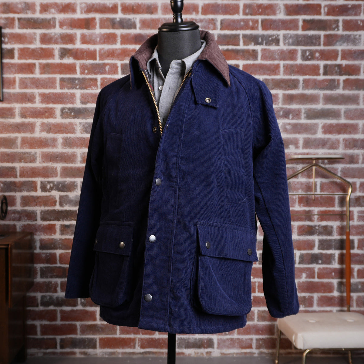 Navy corduroy hunting jacket with a contrasting brown collar displayed on a mannequin against a brick wall.