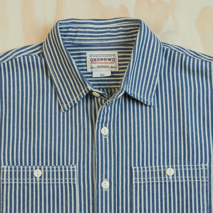 Point collar, OKONKWO neck label and cream buttons on the blue and ecru hickory stripe shirt.