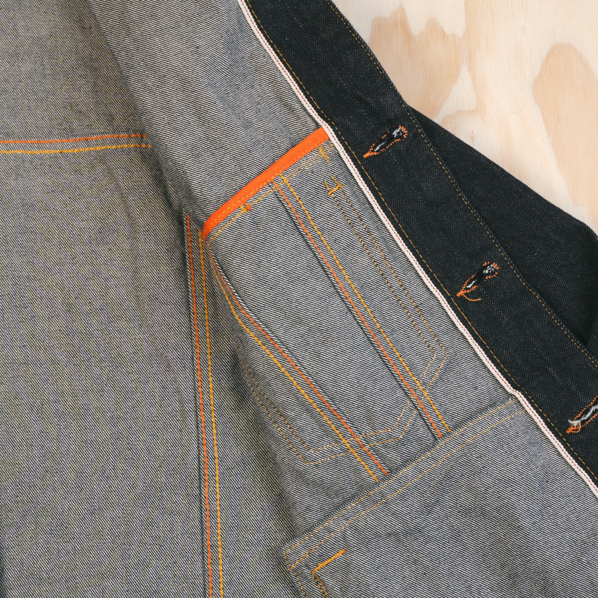 Close-up of a selvedge denim jacket showing the interior and pocket construction, such as flat felled seams, and selvedge id on the button placket.