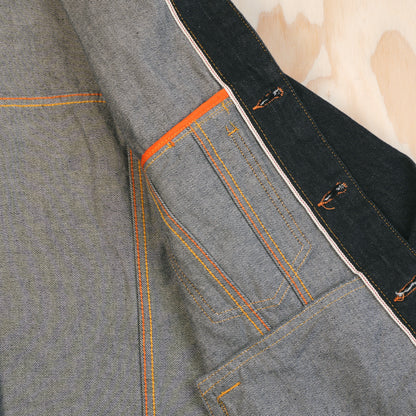 Close-up of a selvedge denim jacket showing the interior and pocket construction, such as flat felled seams, and selvedge id on the button placket.